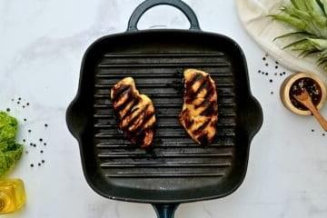 Zwei marinierte Hähnchenbrüste auf einer Grillplatte.