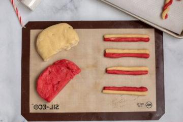 Rote und weiße Plätzchenteigrollen abwechselnd auf einer Silikonbackmatte.