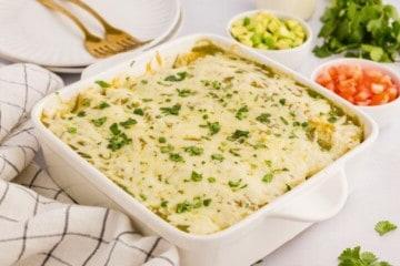 Gebackene grüne Salsa-Hähnchen-Enchiladas in einer weißen Auflaufform, garniert mit gehacktem Koriander.