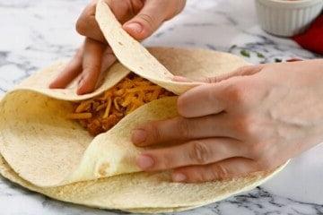 Hände falten die Seiten der Tortilla ein, um die Burrito-Füllung zu bedecken.