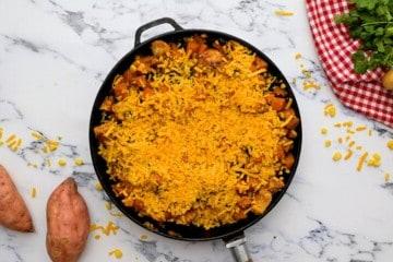 Hähnchen-Süßkartoffel-Pfanne mit geriebenem Käse belegt.