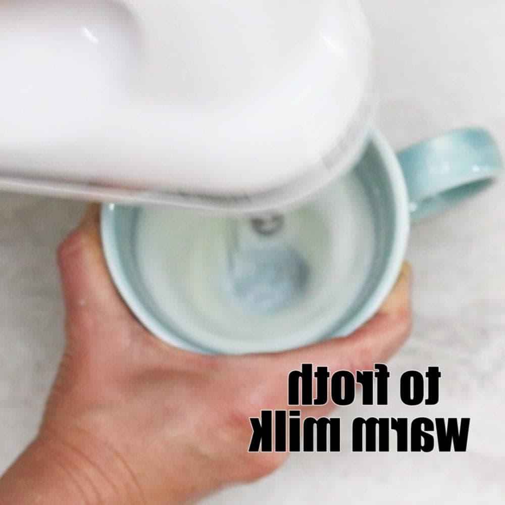 Küchenmixer schäumt Milch in blauer Tasse auf. Text: Warme Milch aufschäumen.