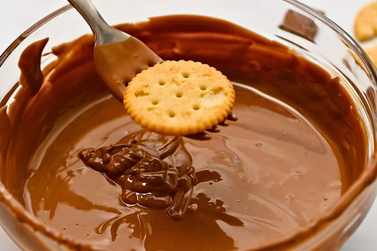 Buttercracker auf einer Gabel wird in geschmolzene, mit Minzextrakt aromatisierte Schokolade getaucht.