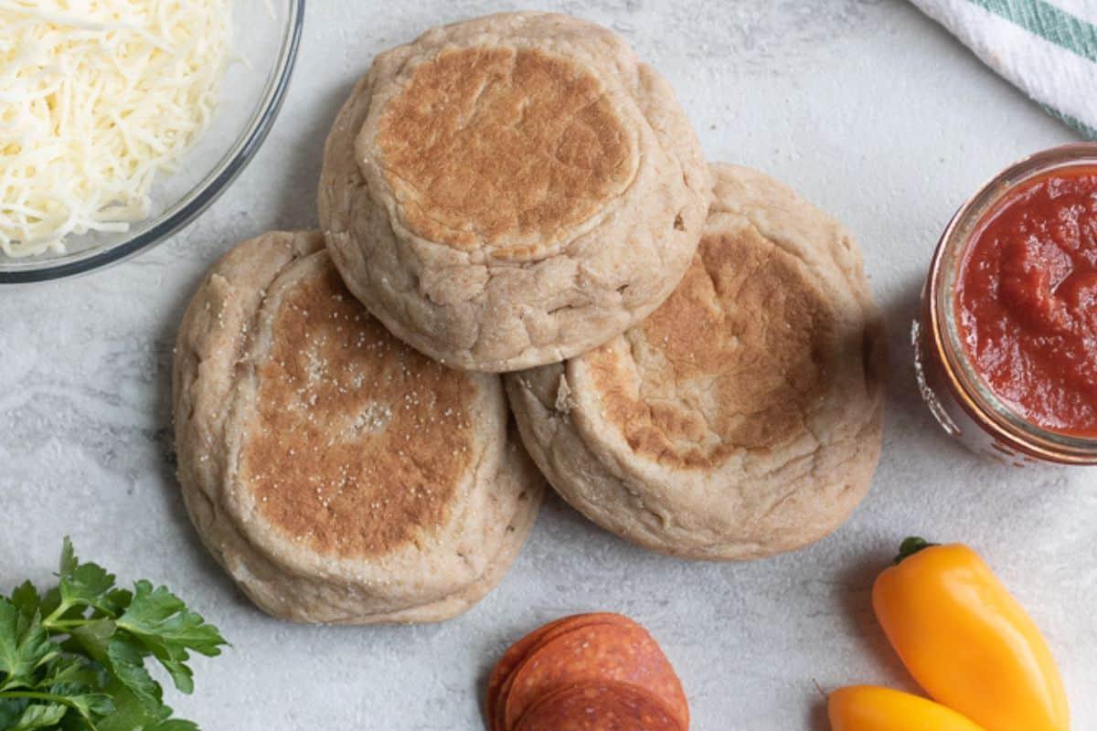 English Muffins, Pizzasauce und geriebener Käse auf einer Arbeitsplatte.