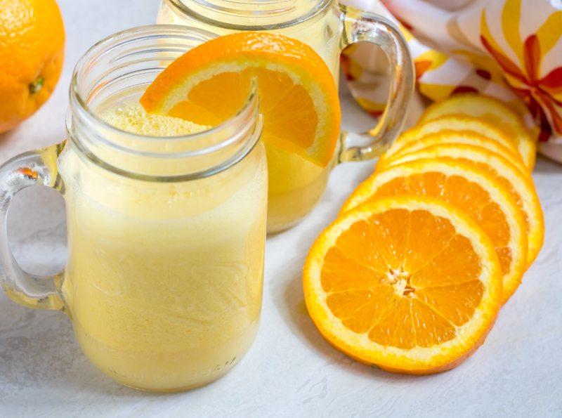 Hausgemachter Orange Julius auf der Arbeitsplatte mit frischen Orangenscheiben.
