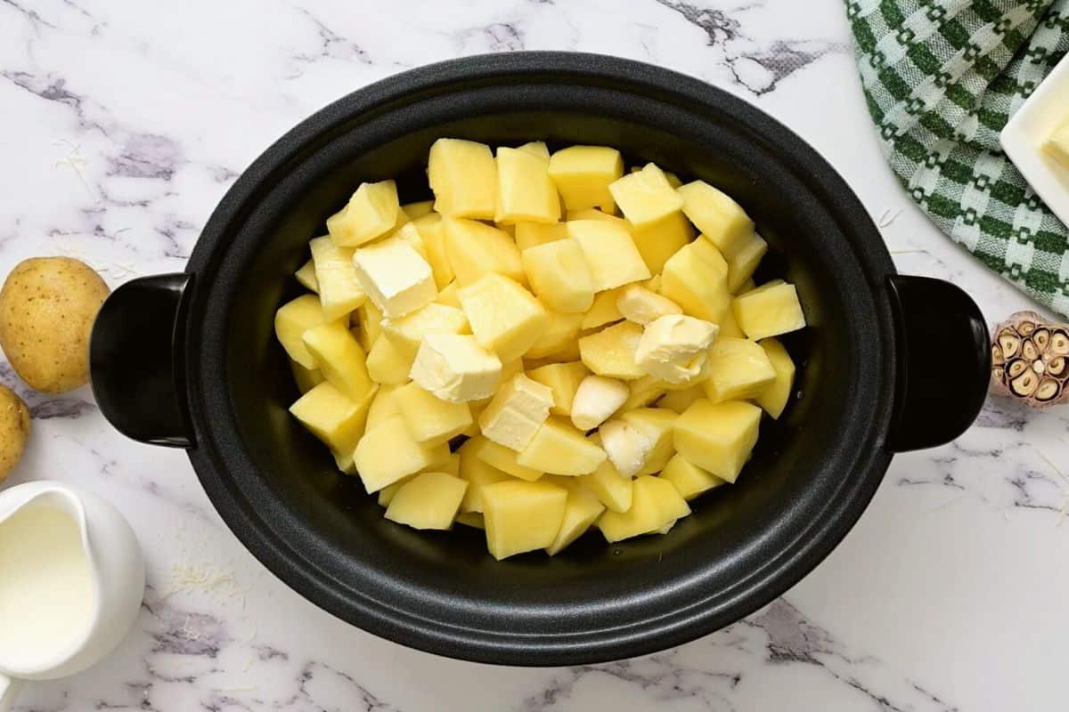 Gewürfelte Kartoffeln, Butter, Brühe und Knoblauch im Slow Cooker.