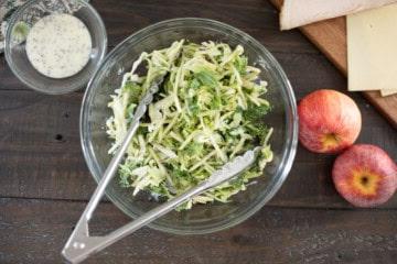 Brokkoli-Slaw und gehackter Grünkohl vermischt mit Mohn-Dressing neben Äpfeln und Cheddar-Käse.
