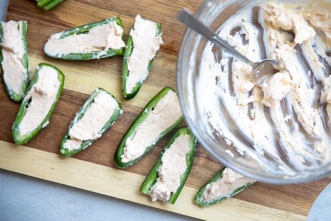 Mit Frischkäsefüllung gefüllte Jalapeños auf einem Schneidebrett, bereit zum Einwickeln.