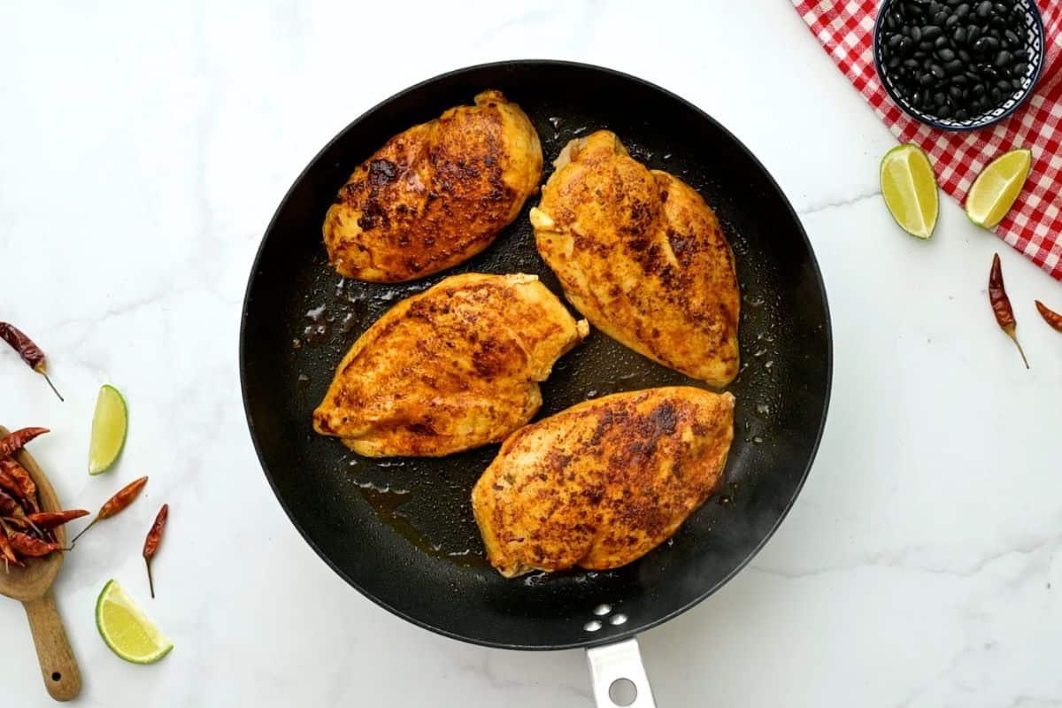 Santa Fe Hähnchen Rezept Vier angebratene gewürzte Hähnchenbrustfilets in einer großen Pfanne für das Cowboy Hähnchen Rezept.