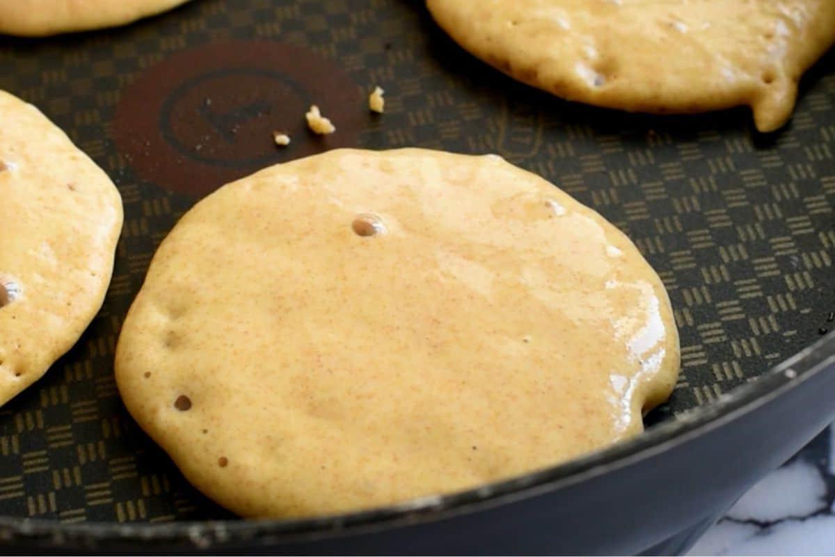 Vollkornpfannkuchen in der Pfanne mit kleinen Bläschen auf der Oberfläche.
