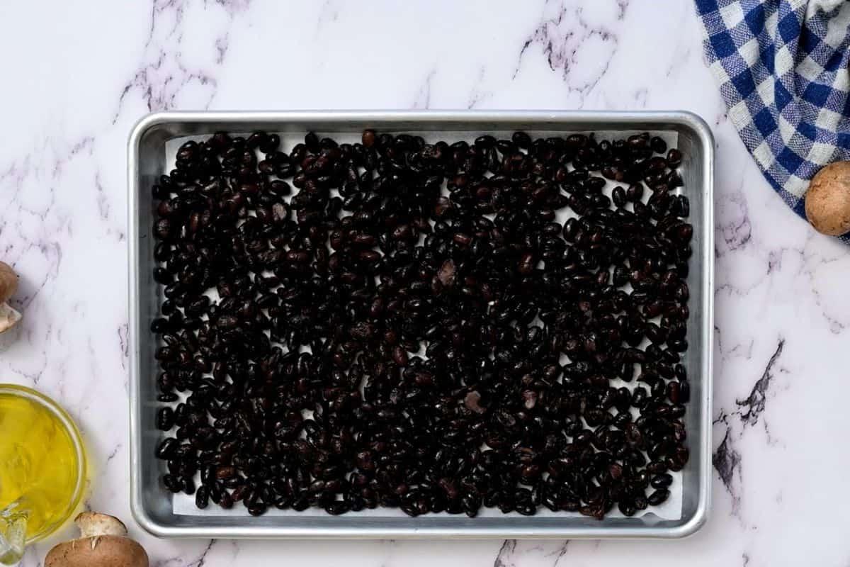Schwarze Bohnen auf einem Backblech mit Backpapier ausgebreitet.