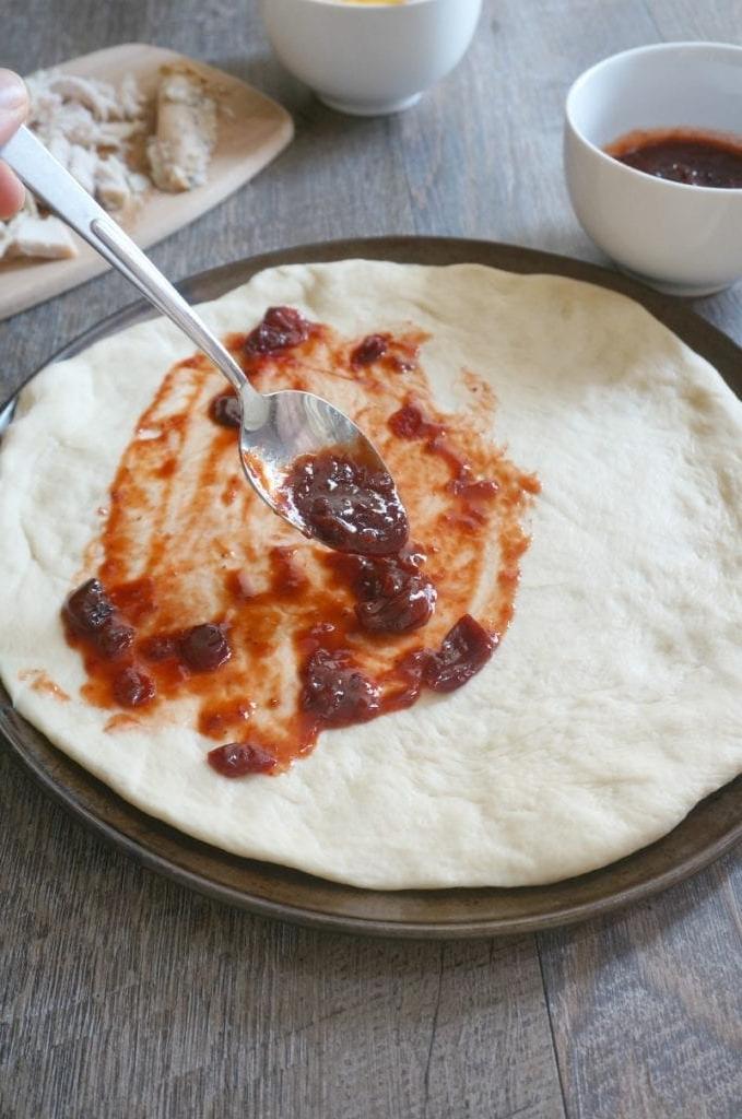 BBQ Preiselbeersauce auf Pizzateig mit Belägen im Hintergrund.