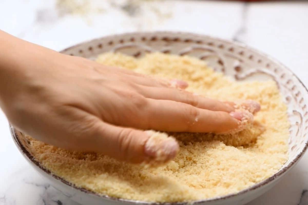 Hand pushing chicken strips into breading.