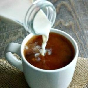 Selbstgemachter Kaffeeweißer wird in einen weißen Kaffeebecher gegossen.