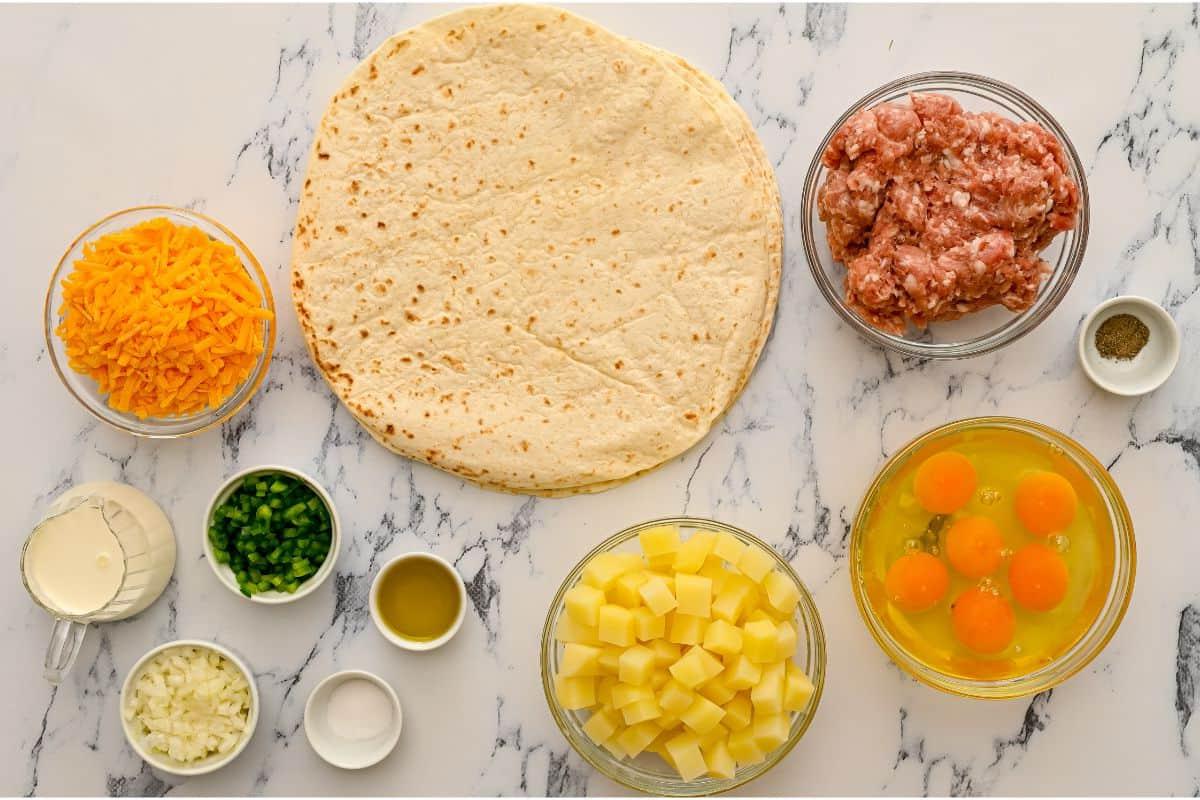 Tortillas, Eier, Kartoffeln, Sahne, Käse, Zwiebeln, Paprika und Wurst auf der Arbeitsfläche.