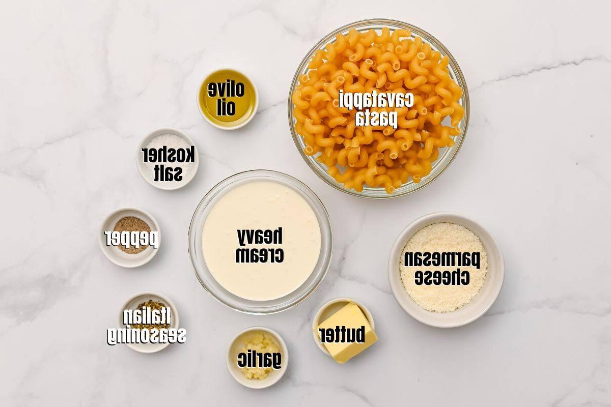 Ausgelegte Zutaten für Cavatappi mit Sahnesoße auf einer Küchenarbeitsplatte, beschriftet und übersichtlich angeordnet.