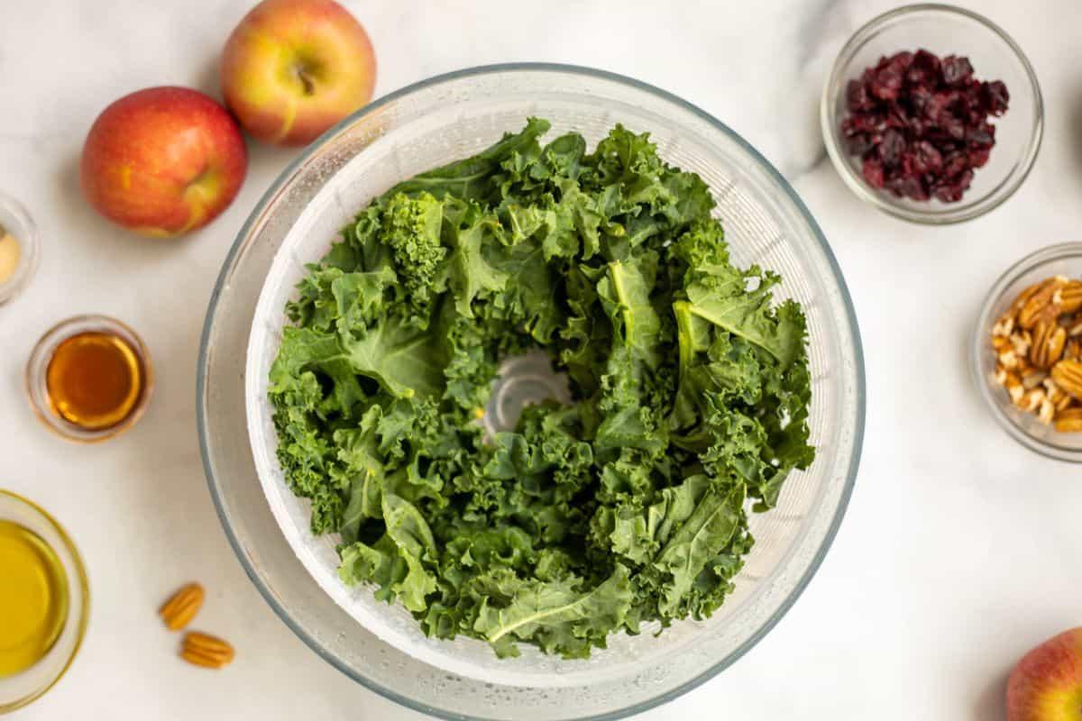 Gerissene Grünkohlblätter in Salatschleuder neben Zutaten für Dressing.