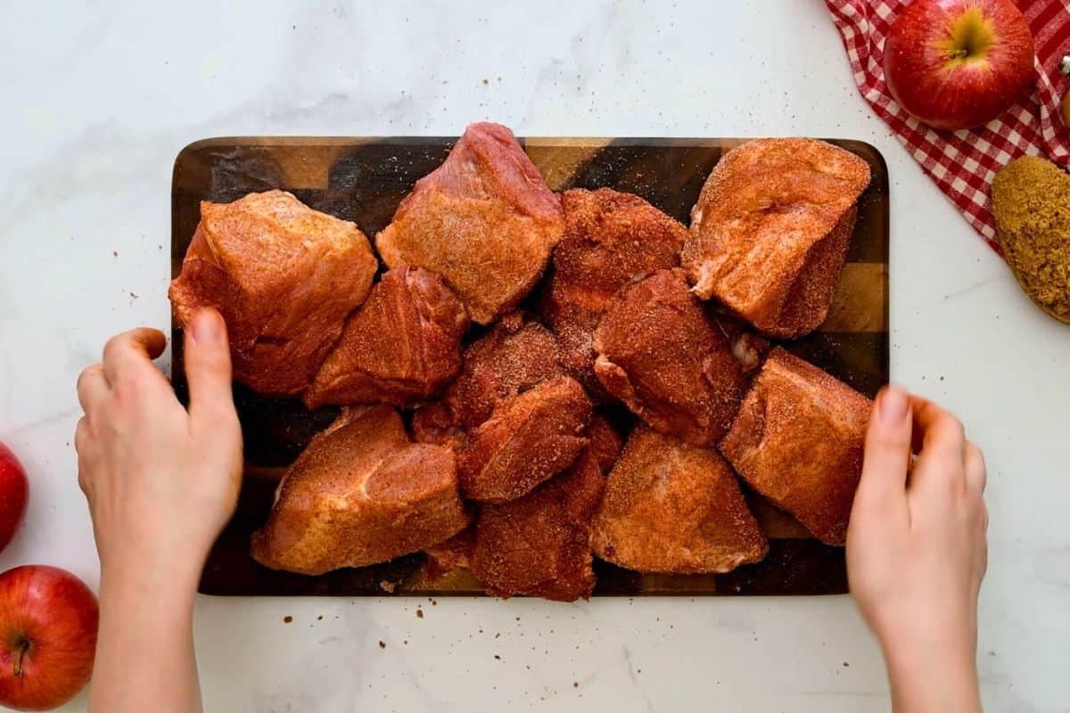 Große Stücke Schweinenacken, gewürzt mit Trockenmarinade, auf einem Schneidebrett.