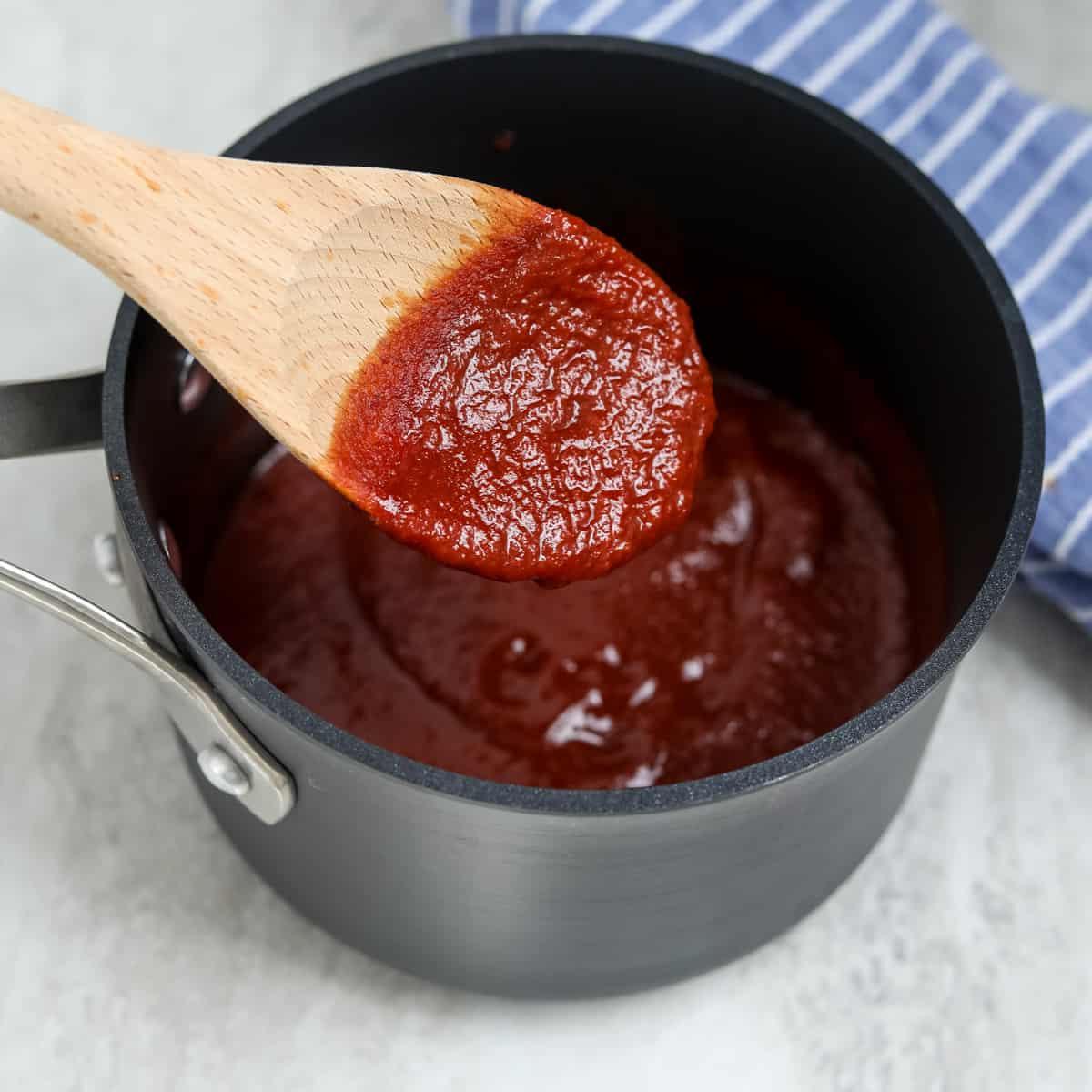 Holzlöffel rührt Barbecue-Sauce in einem Topf um.
