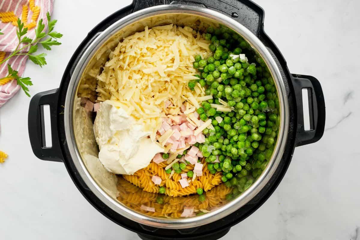 Innentopf des Instant Pots mit gekochten Rotini-Nudeln, Cheddar-Käse, Erbsen, Sauerrahm und gewürfeltem Schinken.