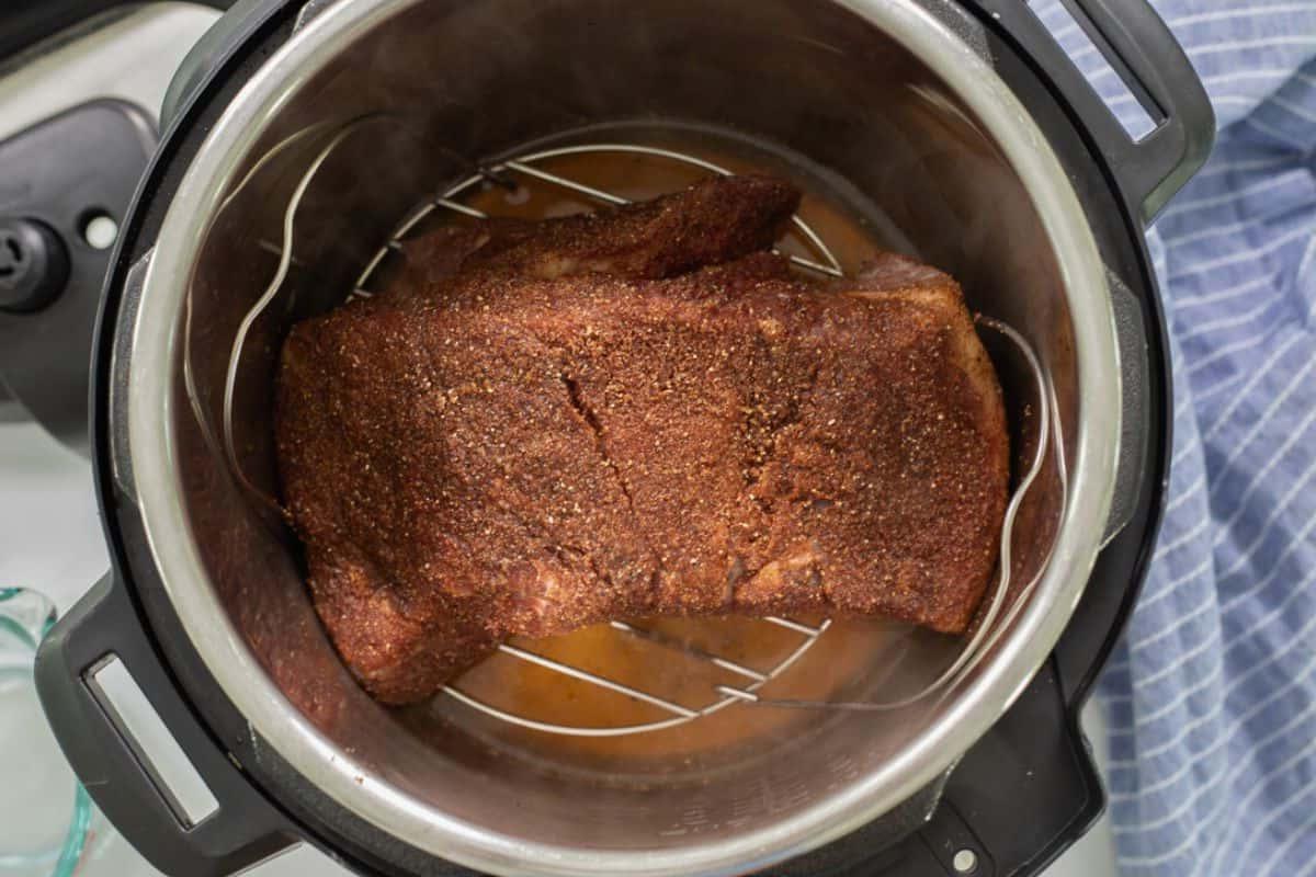 Gewürzte Rinderbrust auf Metalluntersetzer über Apfelsaft im Instant Pot.