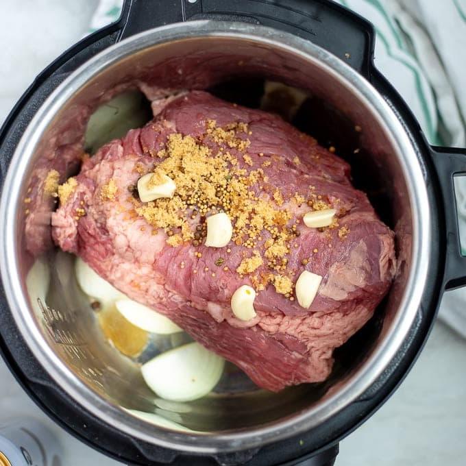 Corned Beef auf Zwiebeln geschichtet und mit Gewürzen im Innentopf des Schnellkochtopfs.