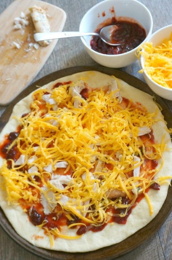 BBQ Pizza bereit, in den Ofen zu gehen, mit allen Belägen im Hintergrund.