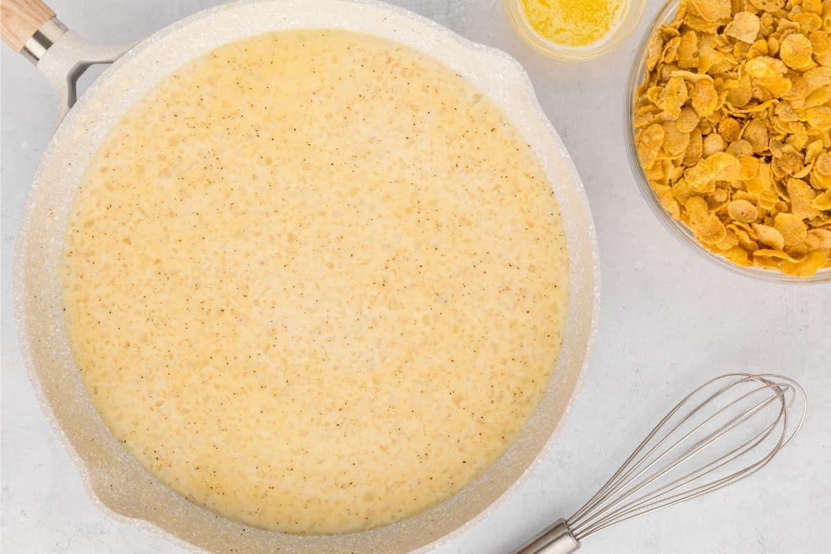 Rezept für hausgemachte Funeral Potatoes Pfanne mit Rahmsauce neben einem Schneebesen.