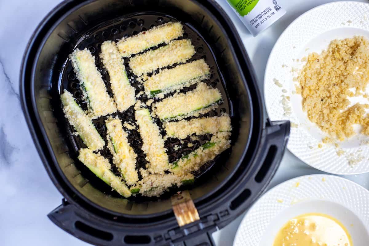 Panierte Zucchini Pommes im Korb der Heißluftfritteuse.
