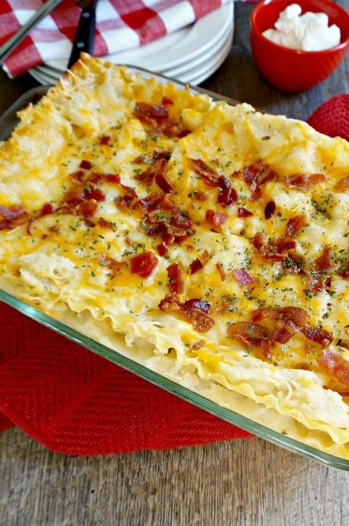 Gebackene Kartoffelpüree Lasagne in Glasauflaufform mit Speck belegt.
