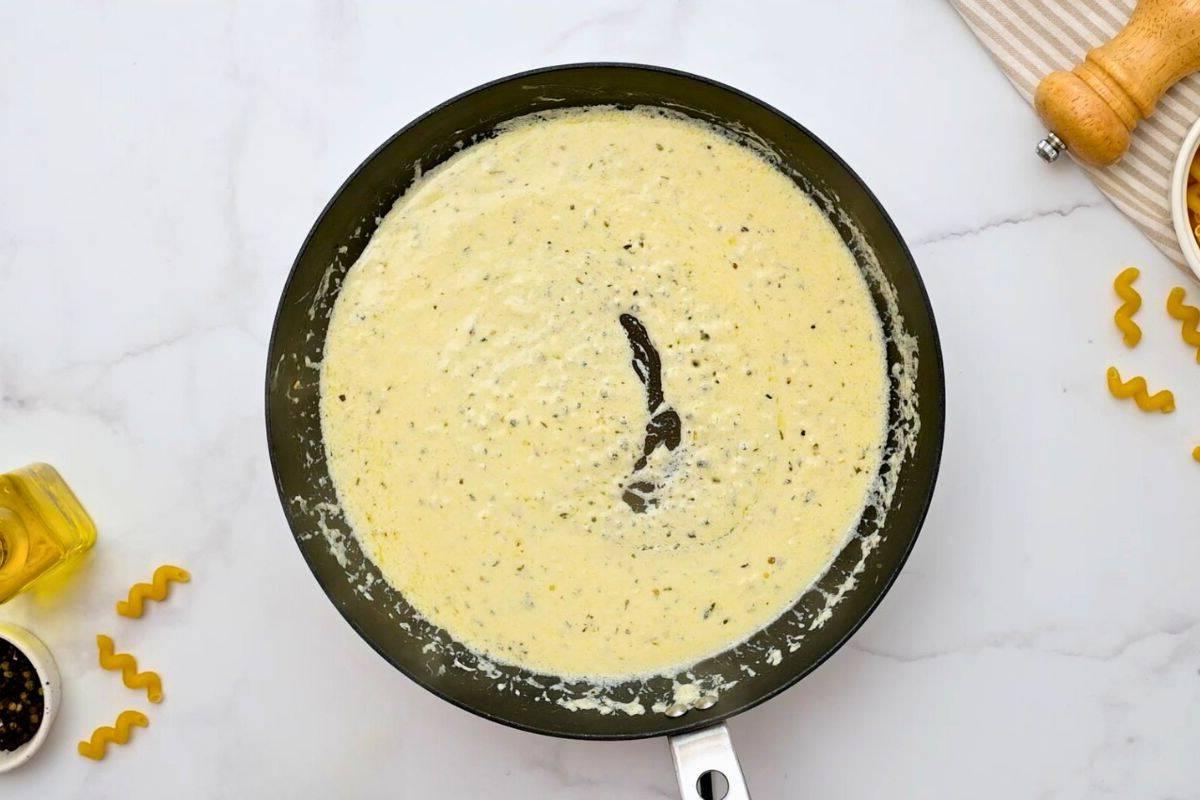 Cremige Soße für Cavatappi Pasta in einer großen Pfanne, zubereitet mit Schlagsahne und frisch geriebenem Parmesan. Die Soße glänzt und sieht appetitlich aus.
