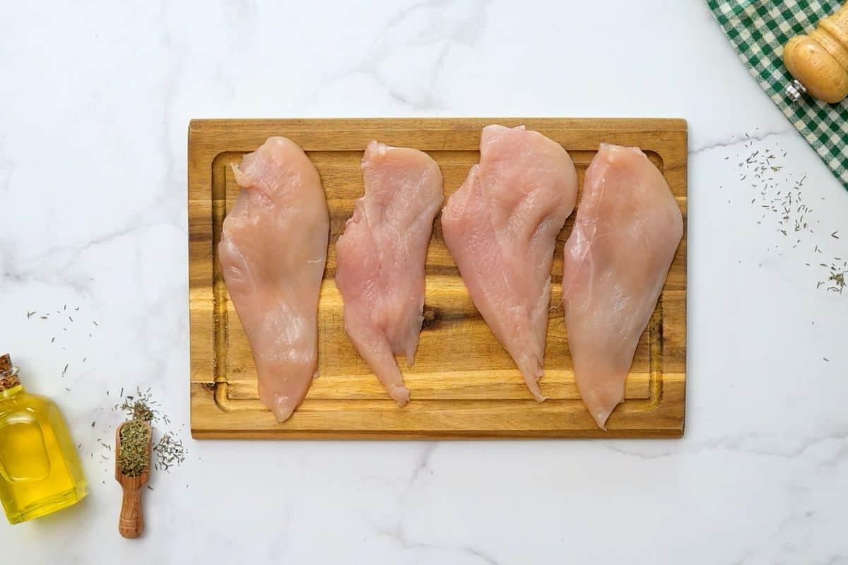 Chicken breasts cut into cutlets on wooden cutting board next to fresh thyme.