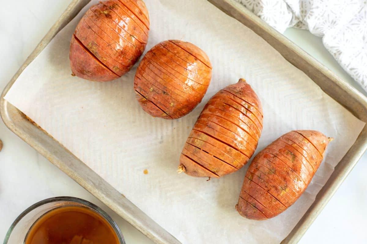 Hasselback Süßkartoffel Rezept Schritt für Schritt Glasierte, geschnittene Süßkartoffeln auf einem mit Backpapier ausgelegten Backblech.