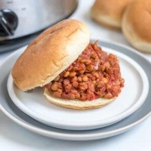 Schongarer-Linsen-Sloppy-Joes 2 Vegane Sloppy Joes mit Linsen auf einem Brötchen auf einem Teller mit dem Slow Cooker im Hintergrund.