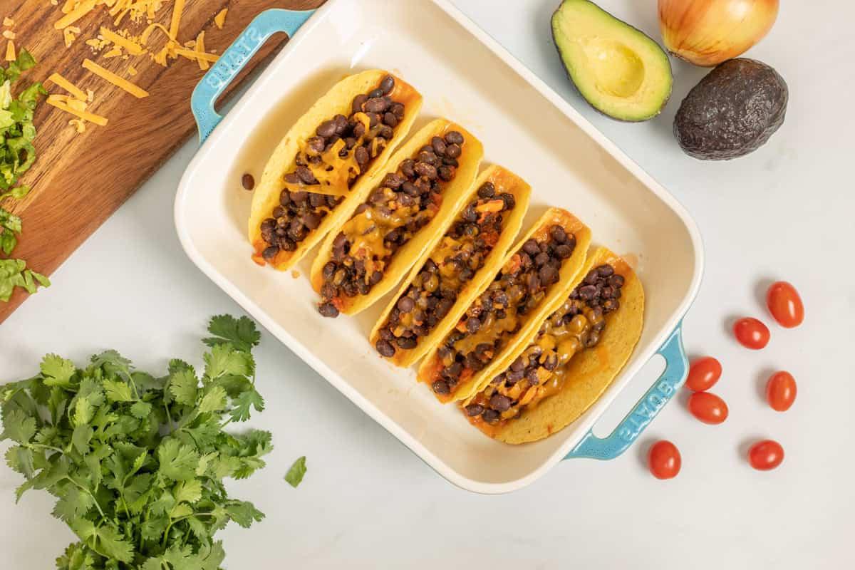 Einfaches Schwarze-Bohnen-Taco-Rezept Schwarze Bohnenfüllung in getoasteten Taco-Schalen, mit geschmolzenem geriebenem Käse belegt.