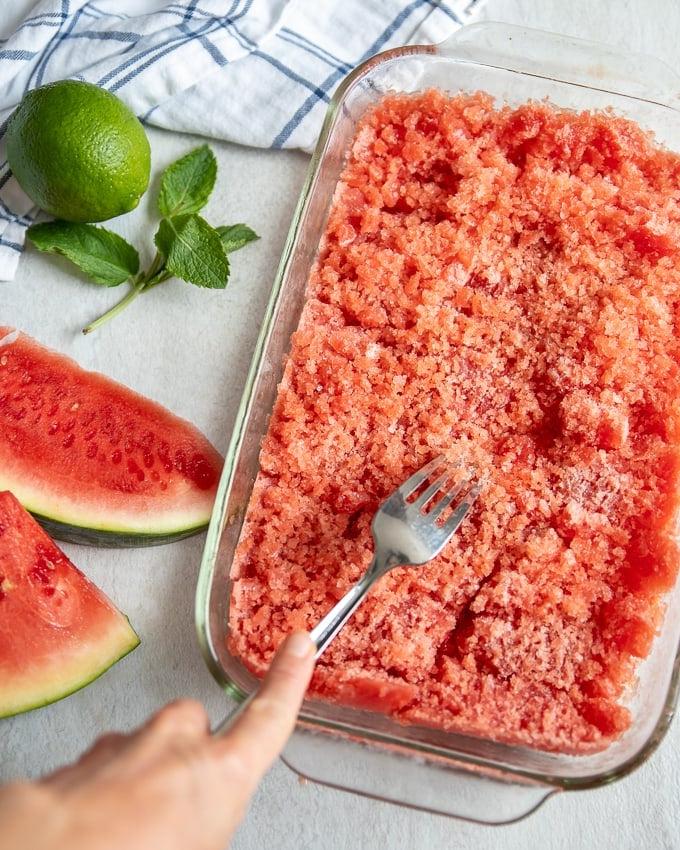 Wie man Granita macht Wassermelonen Granita in einer klaren Glasschale, die das Schaben der Mischung mit einer Gabel zeigt.