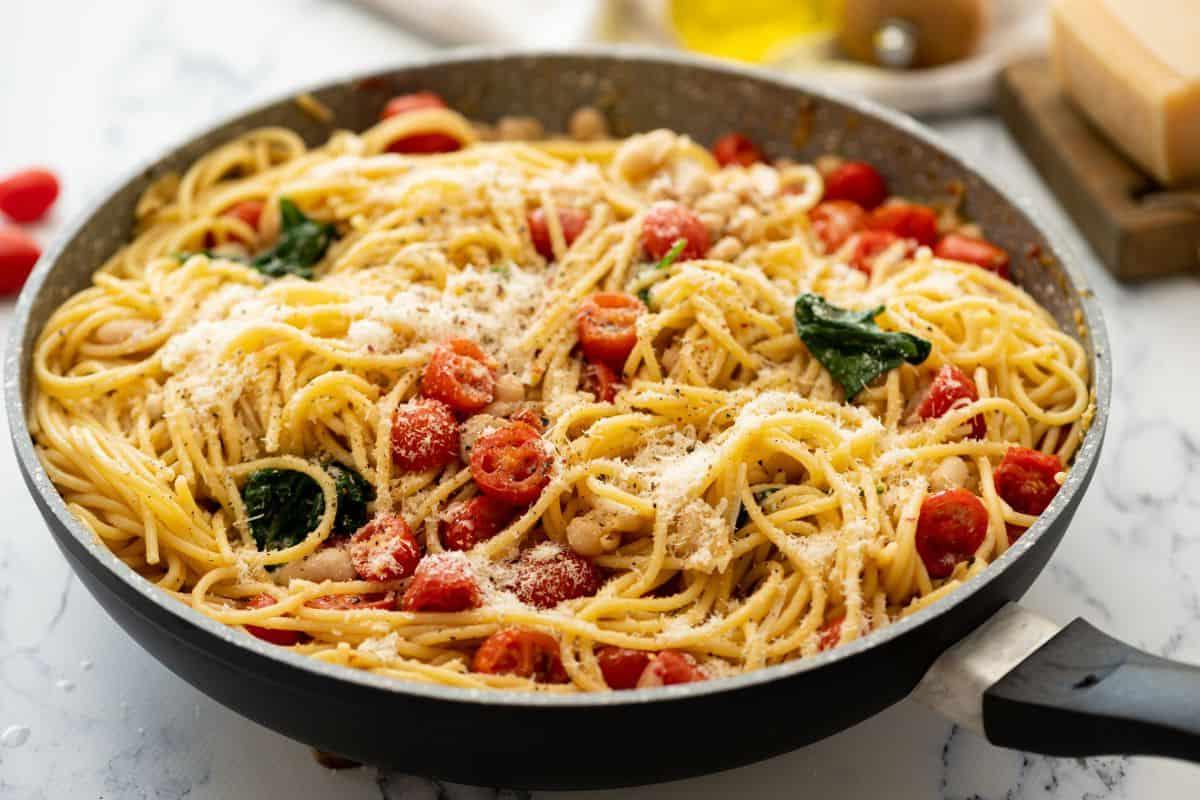 Große Pfanne mit Pasta, weißen Bohnen, Tomaten und Spinat, mit Parmesan bestreut.