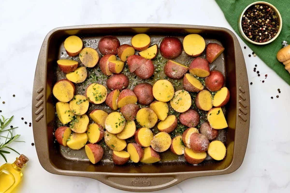Halbierte rote Kartoffeln auf dem Backblech, gewürzt mit Knoblauchpulver, Salz, Pfeffer und Rosmarin.