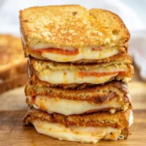 Aufgeschnittener Stapel Pizza Grilled Cheese, aus dem Käse auf einem Schneidebrett quillt.