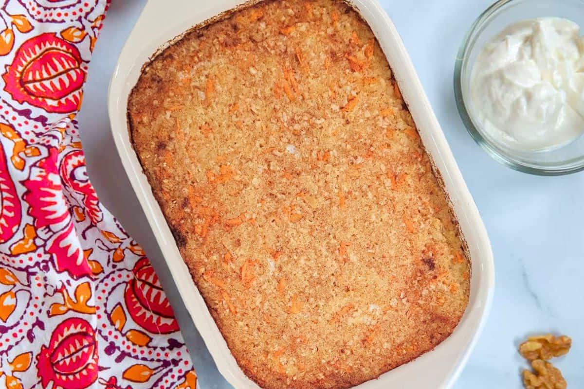 Karottenkuchen-Haferflocken-Auflauf in weißer Auflaufform neben Joghurt und Walnüssen gebacken.