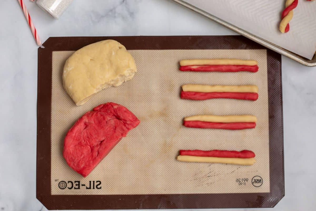 Rote und weiße Plätzchenteigrollen abwechselnd auf einer Backmatte für Weihnachts-Zuckerstangen-Plätzchen.