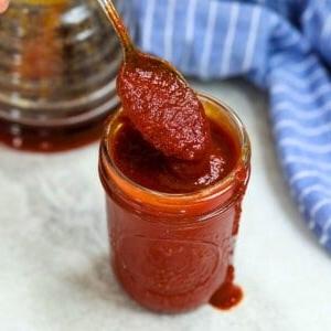 Ein Glas selbstgemachter BBQ-Sauce mit einem Löffel, der herausragt.