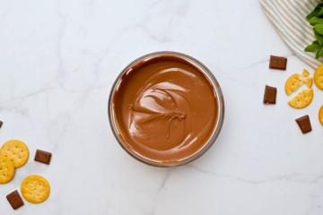 Geschmolzene Schokolade für das Thin Mint Keks Rezept in einer großen Glasschüssel mit Schokolade und Crackern daneben.