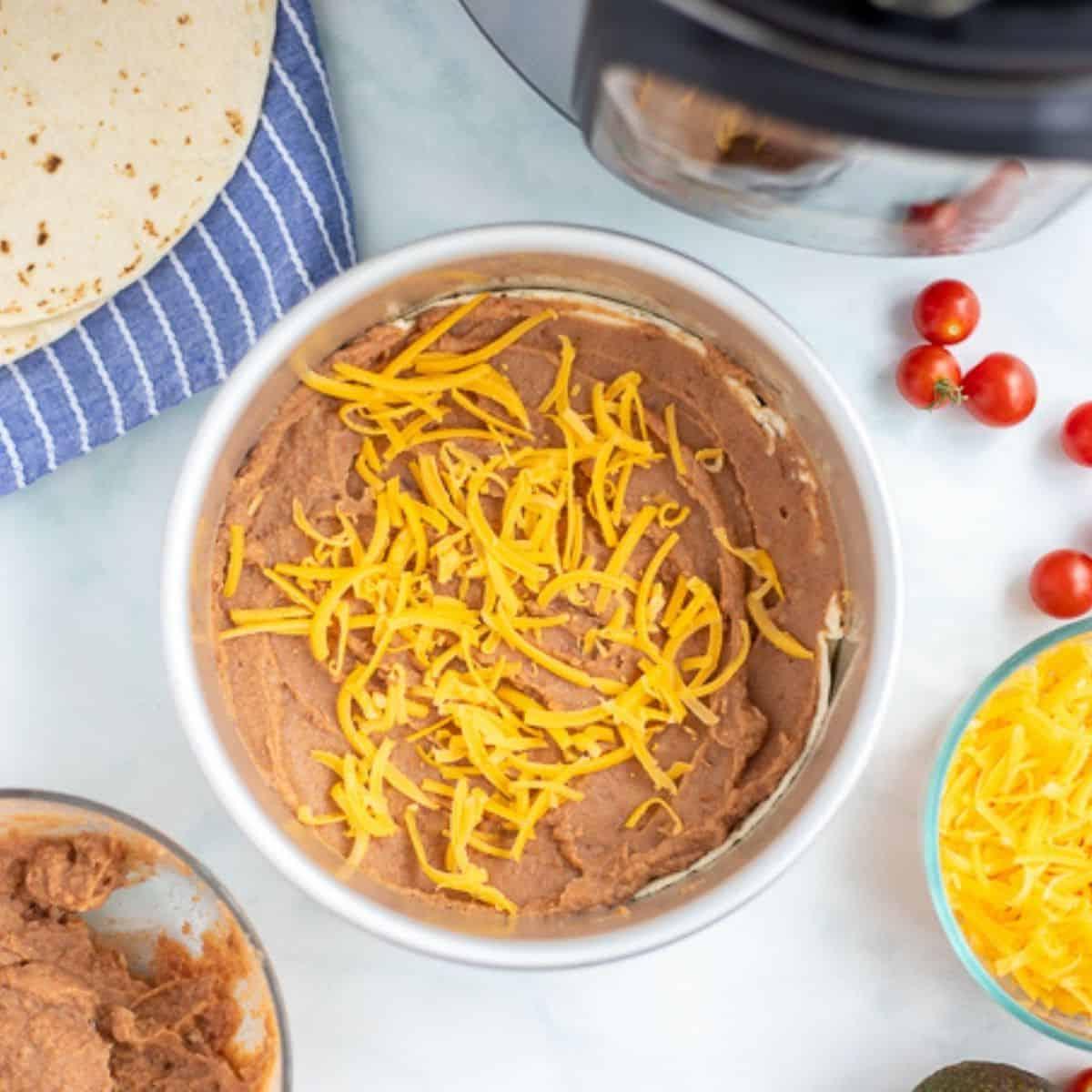 Refried Beans und Käse auf Tortilla neben Instant Pot.