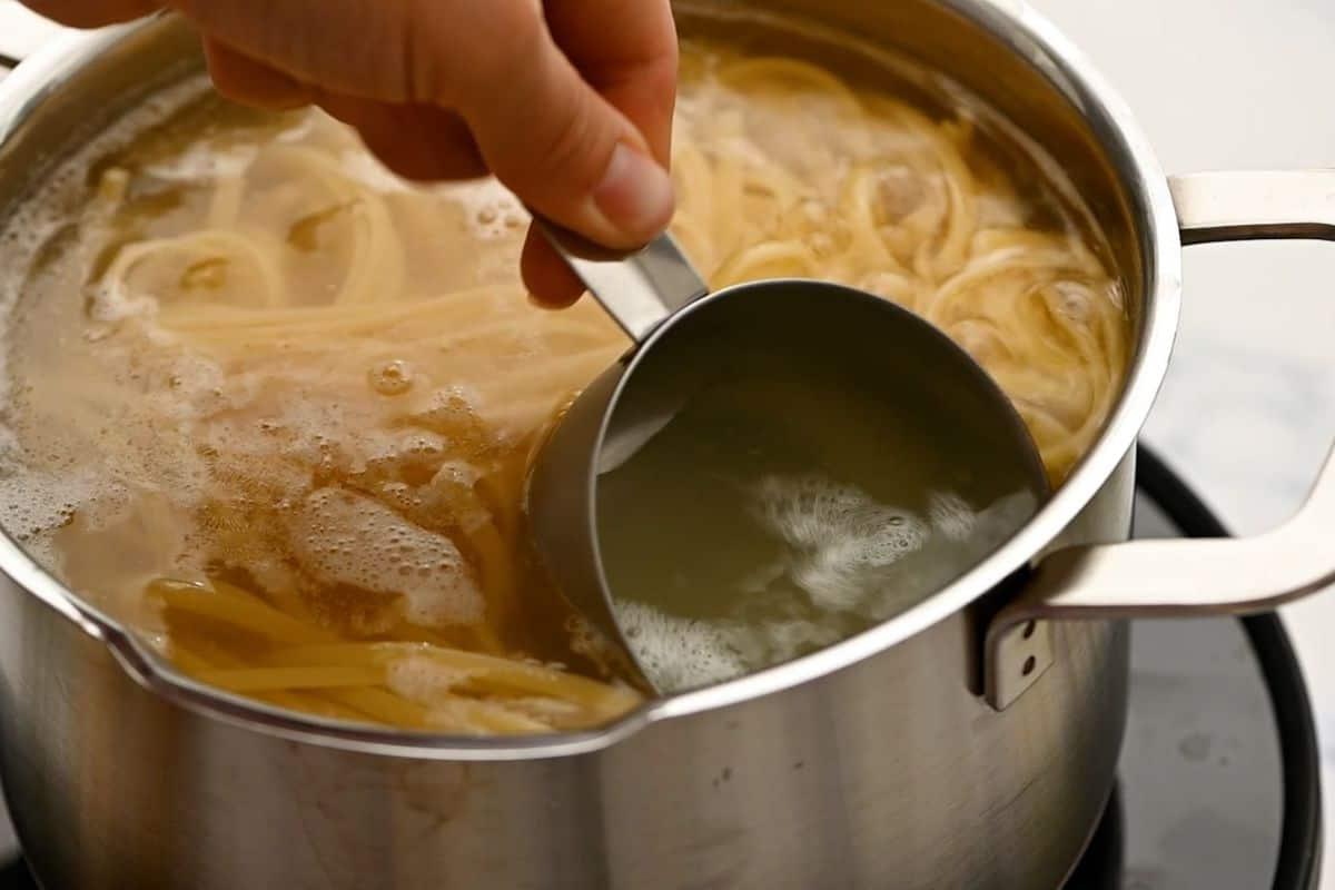 Messbecher schöpft Nudelwasser aus einem Topf, in dem Linguine kocht. Ein wichtiger Schritt für eine cremige Sauce.