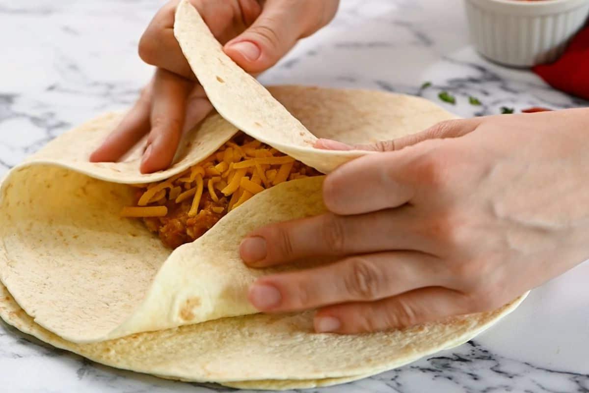 Hände falten die Seiten der Tortilla ein, um die Burrito-Füllung zu bedecken.
