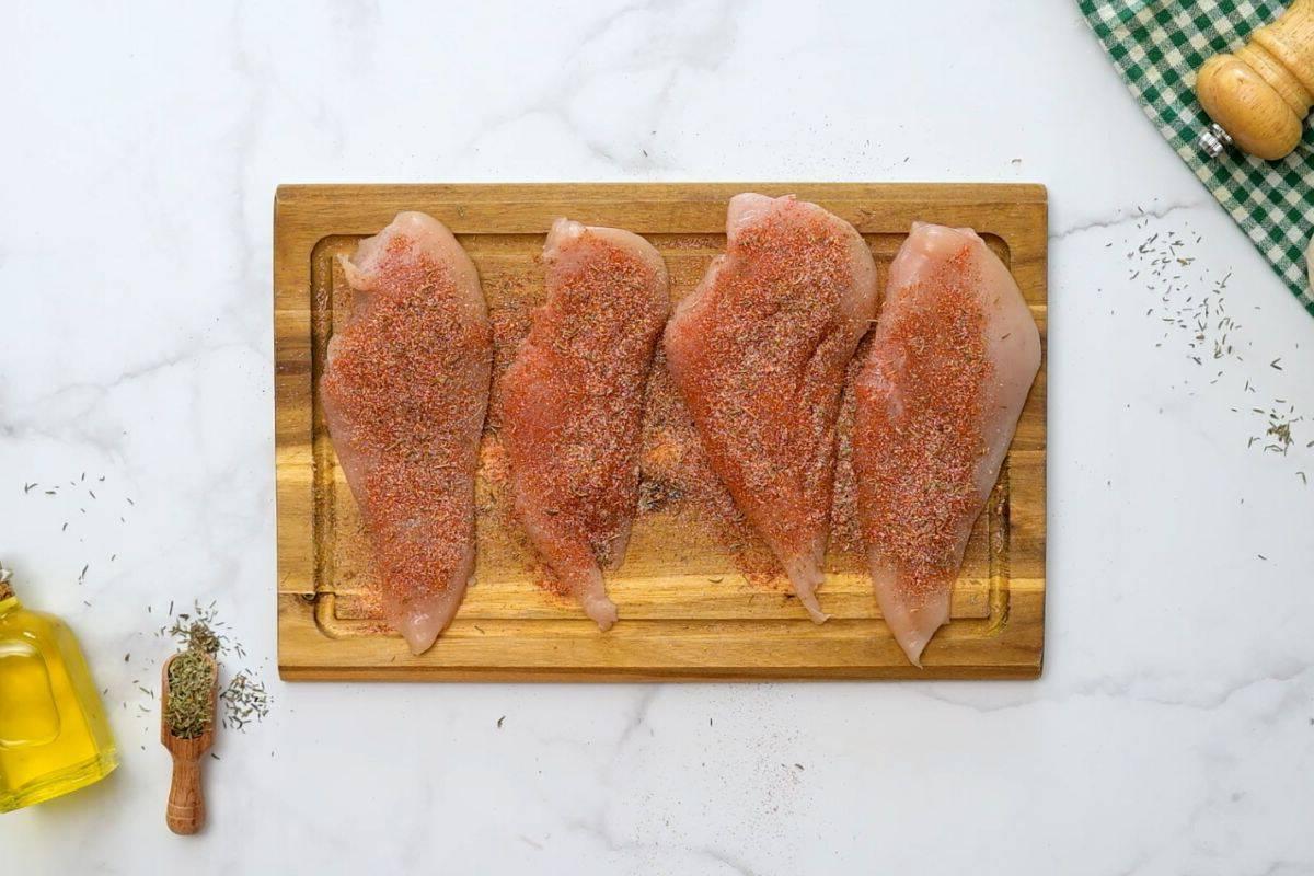 Four chicken cutlets on wooden cutting board sprinkled with Blackened Seasoning Blend.