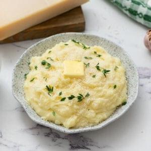 Servierfertiges Kartoffelpüree aus dem Slow Cooker, garniert mit Parmesan, Butter und Thymian.