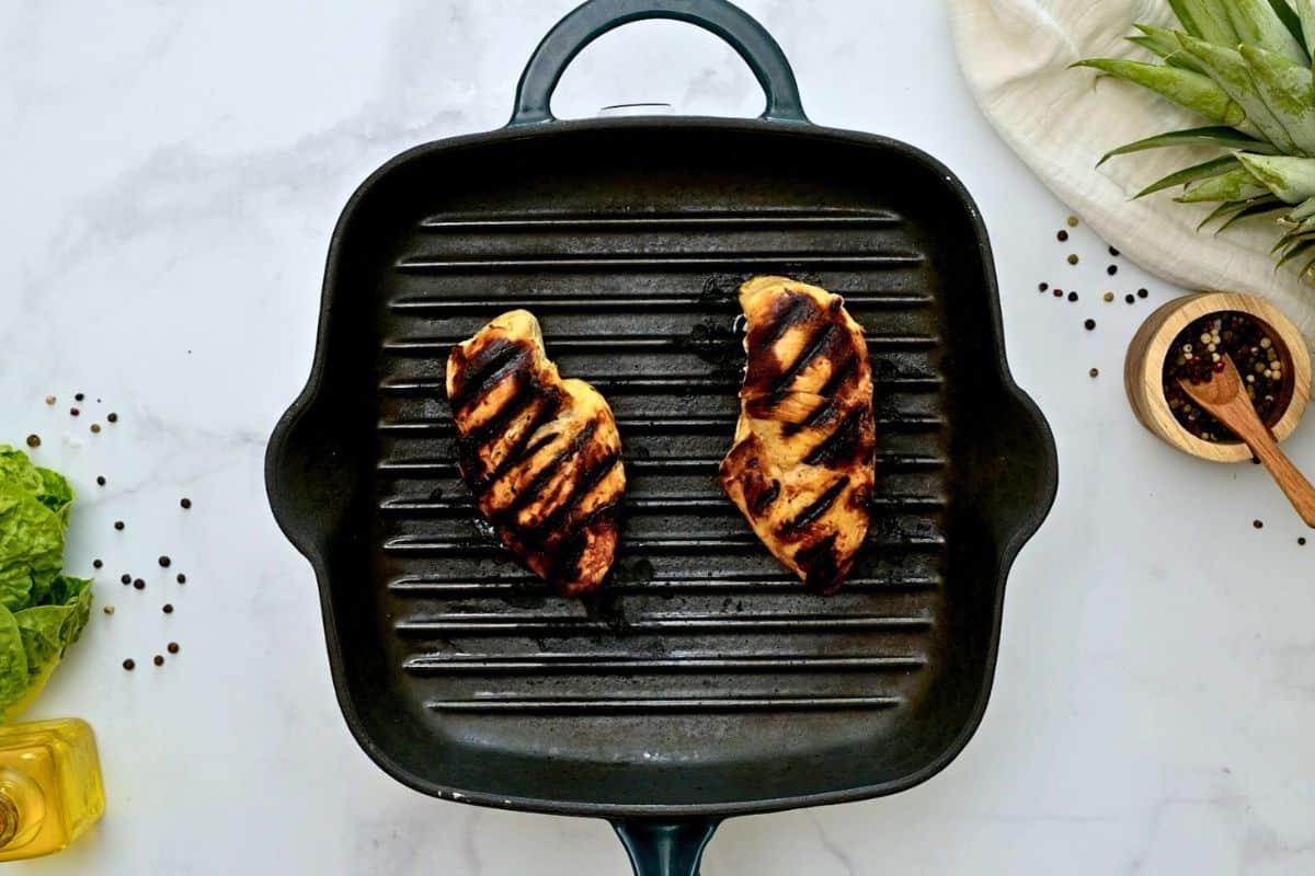Zwei marinierte Hähnchenbrüste auf einer Grillplatte.