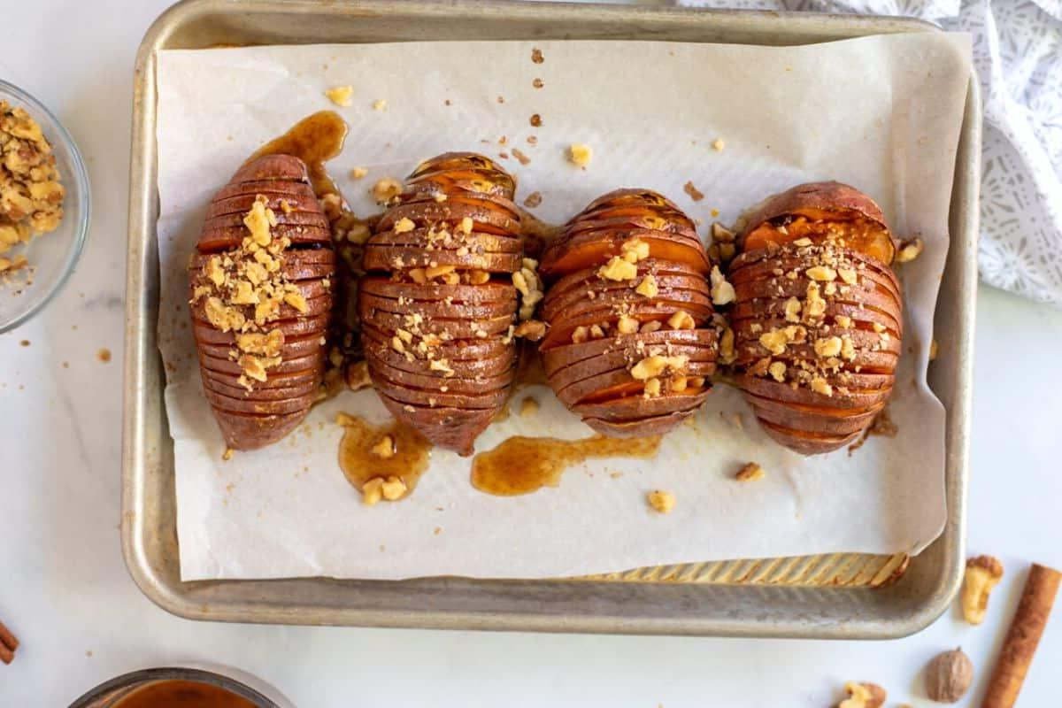 Glasierte Süßkartoffeln im Ofen Hasselback Süßkartoffeln auf dem Backblech, nachdem sie glasiert und mit Nüssen belegt wurden.